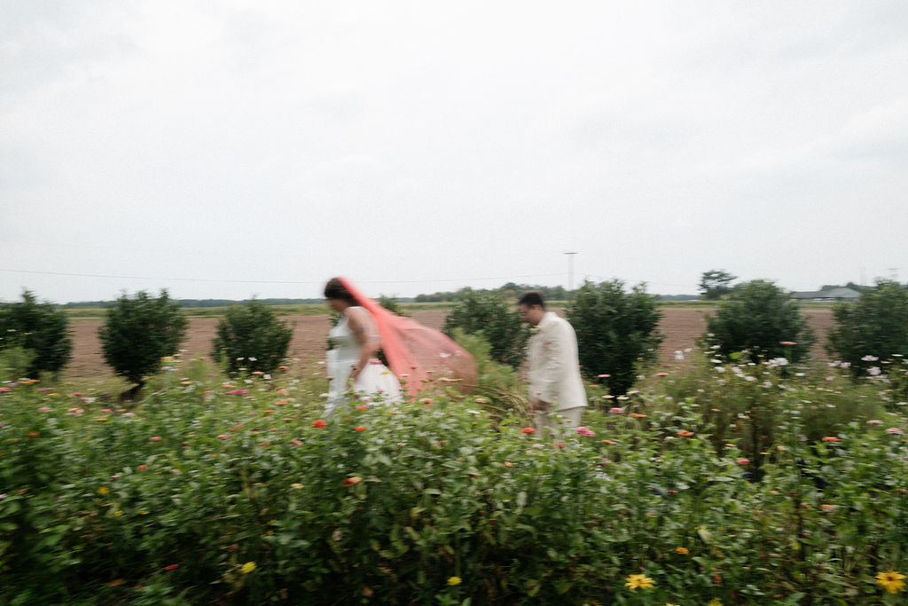 Wedding couple walking through field of wildflowers at outdoor wedding.